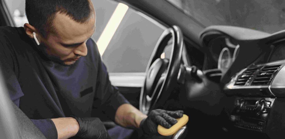 Man in a garage. Worker polish inside a car. Man in a black uniform.